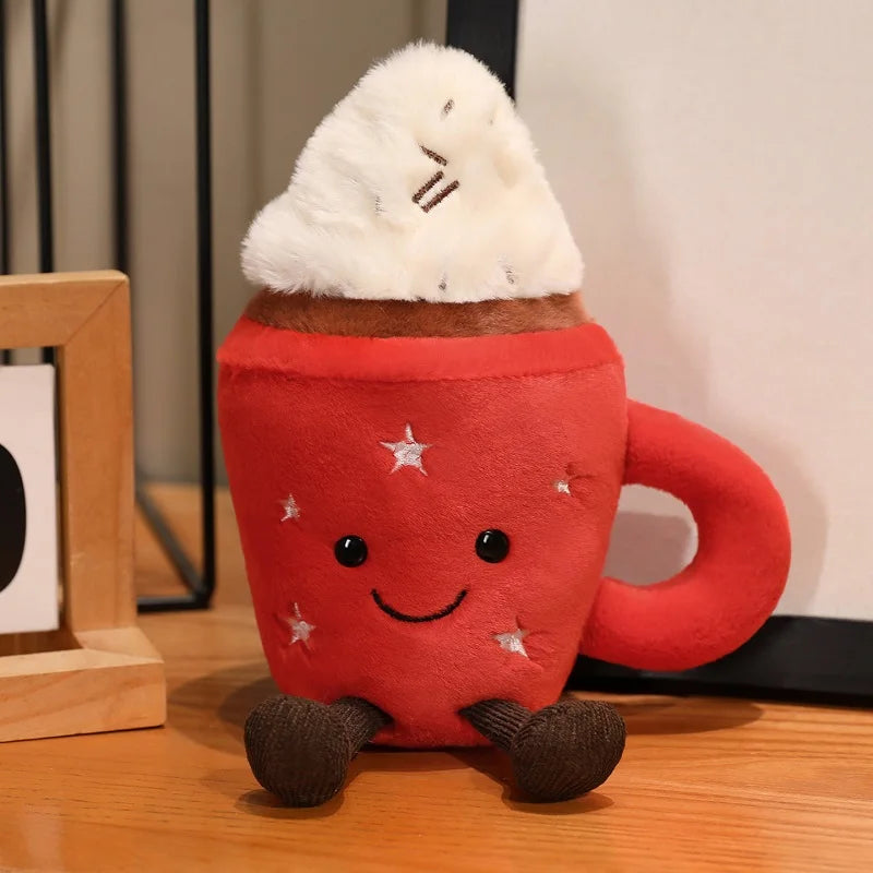 Cute cocoa plushie sitting on a wooden desk next to a real mug of hot cocoa