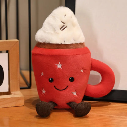 Cute cocoa plushie sitting on a wooden desk next to a real mug of hot cocoa