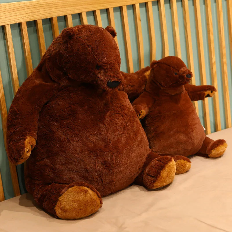 Giant brown bear stuffed animal sitting on a gray sofa in couch potato pose against neutral backdrop