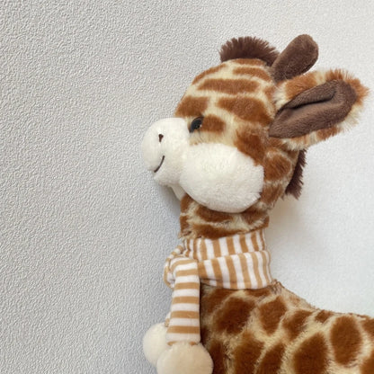 Giraffe plushie sitting upright showing nursery decor styling on a wooden shelf