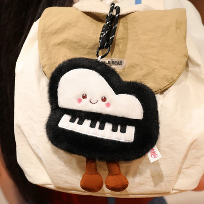 Mini kawaii bag charm piano plushie hanging from a backpack zipper alongside other keychain charms