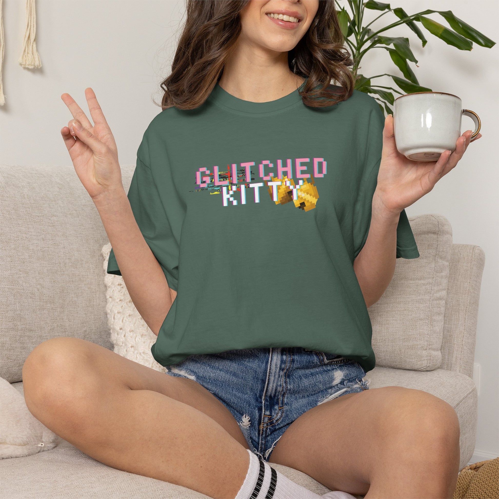 Person wearing a green t-shirt with 'GLITCHED KITTY' text, sitting on a couch holding a mug.