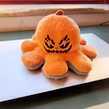 Reversible Halloween plush sitting on a shelf display alongside seasonal decor, spooky cute stuffed toy