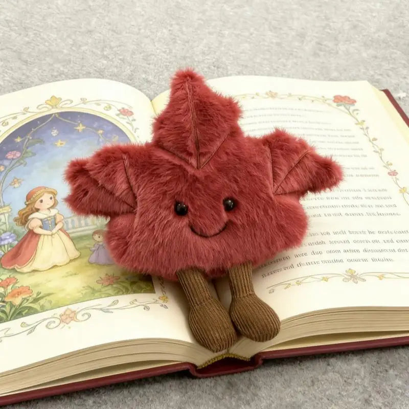Smiling maple leaf plushie displayed on wooden shelf with seasonal fall decor accents